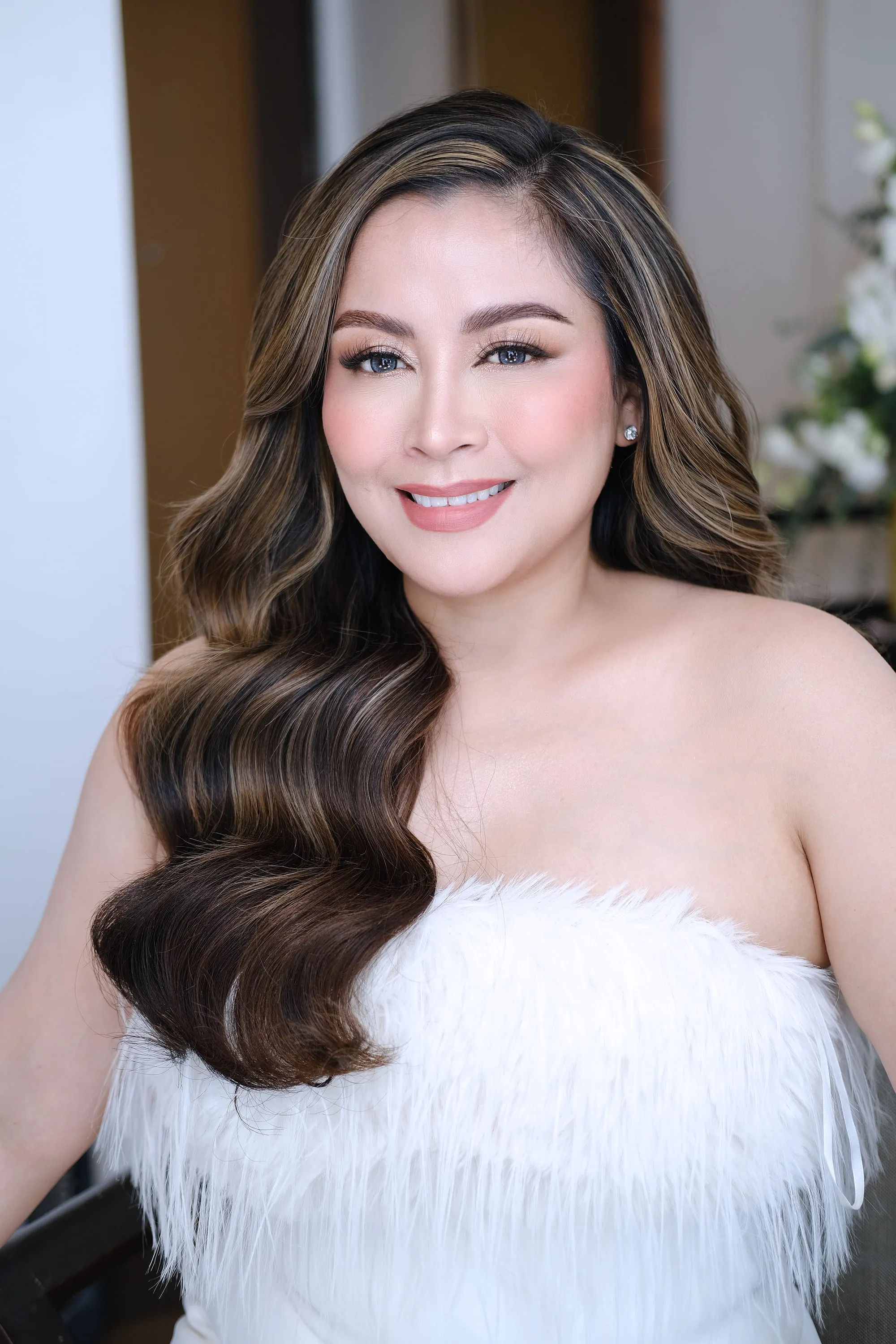 Bridal make-up with a warm peach blush and softly blended brown shadow, worn with brushed-out waves and a white feathered bodice.