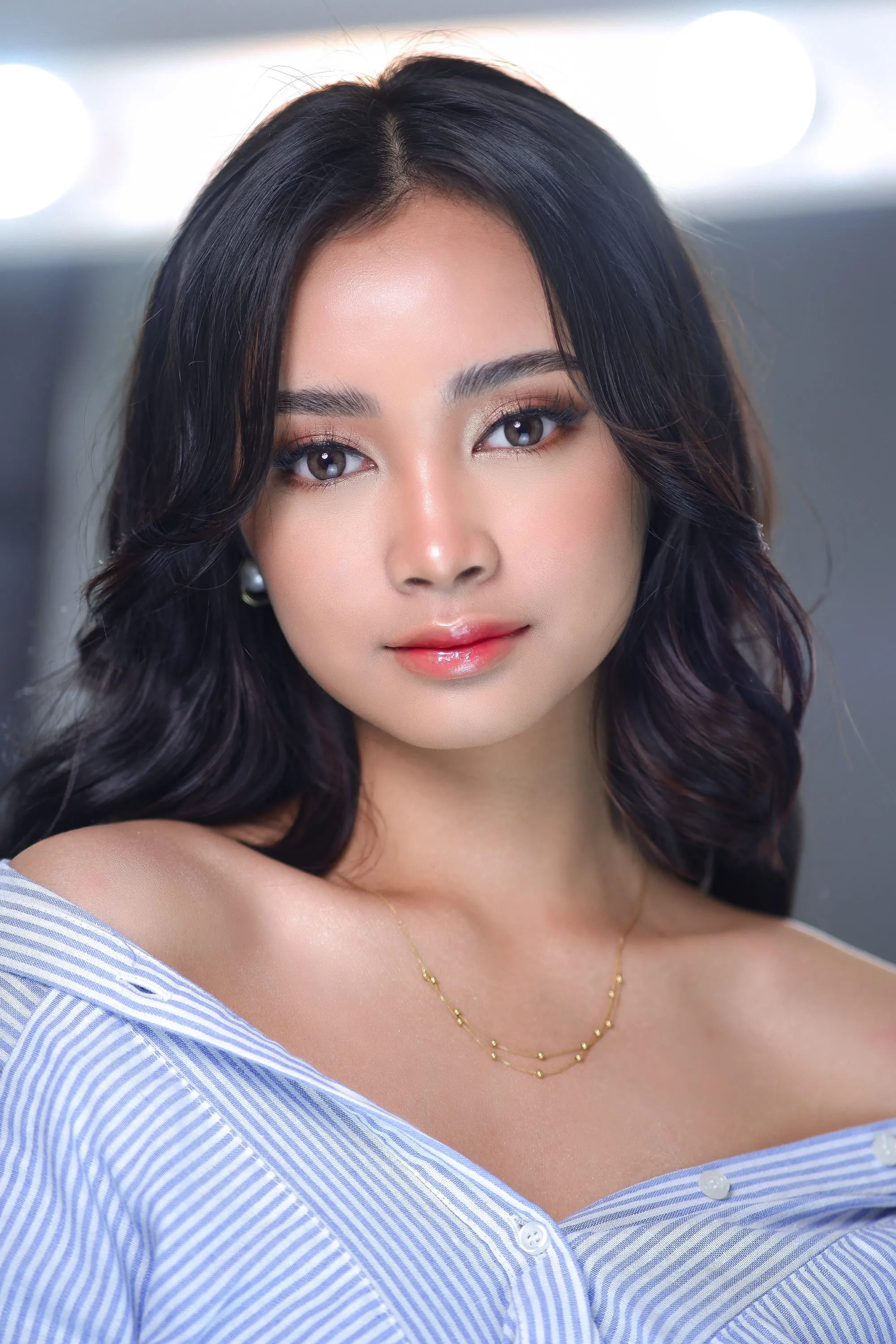 Editorial make-up with a bare skin finish, softly blended brown shadow and a glossy lip, worn with a striped shirt off one shoulder.