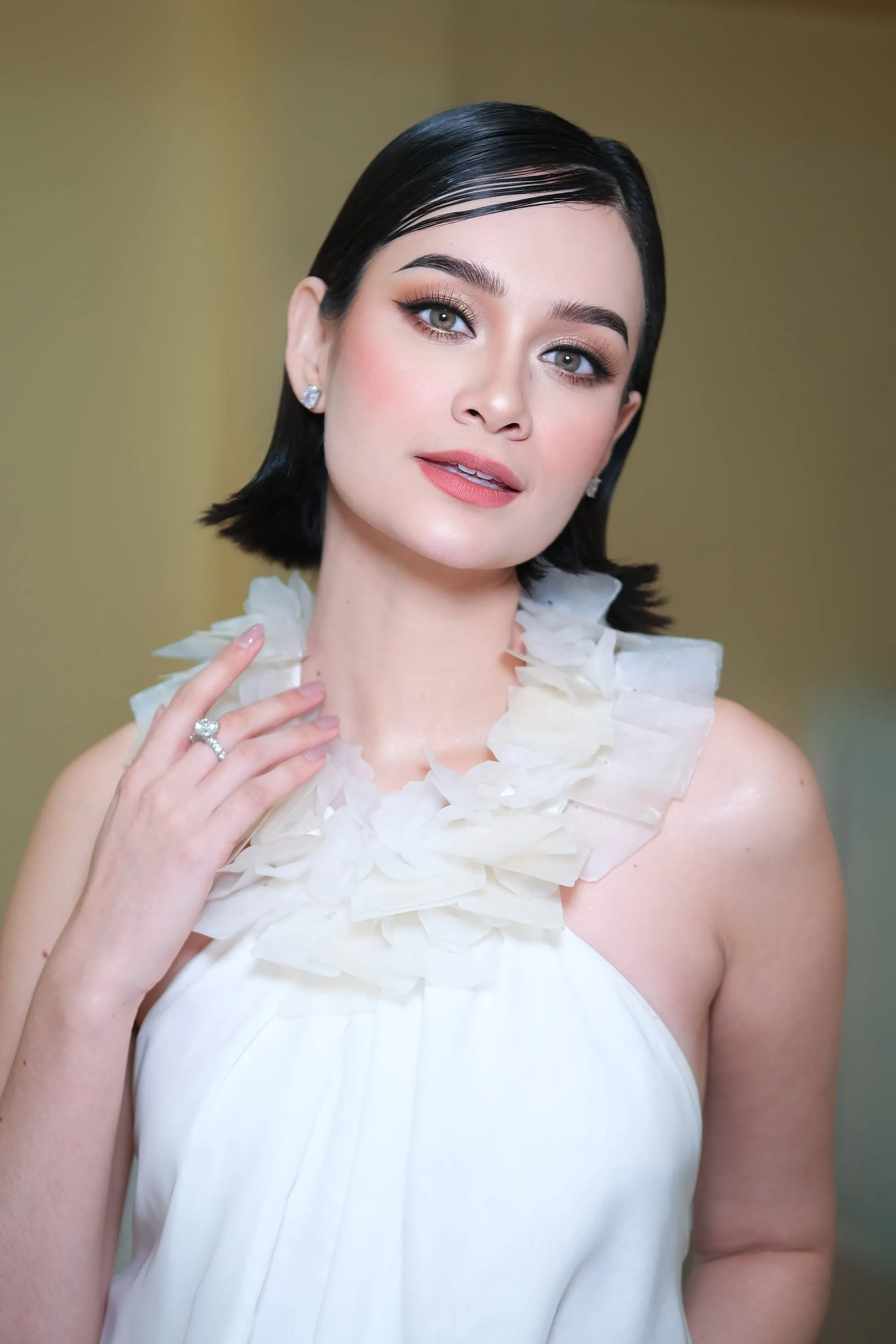 Editorial make-up with a sharp lash line and a muted rose lip, worn with a chin-length bob and an ivory ruffled collar.