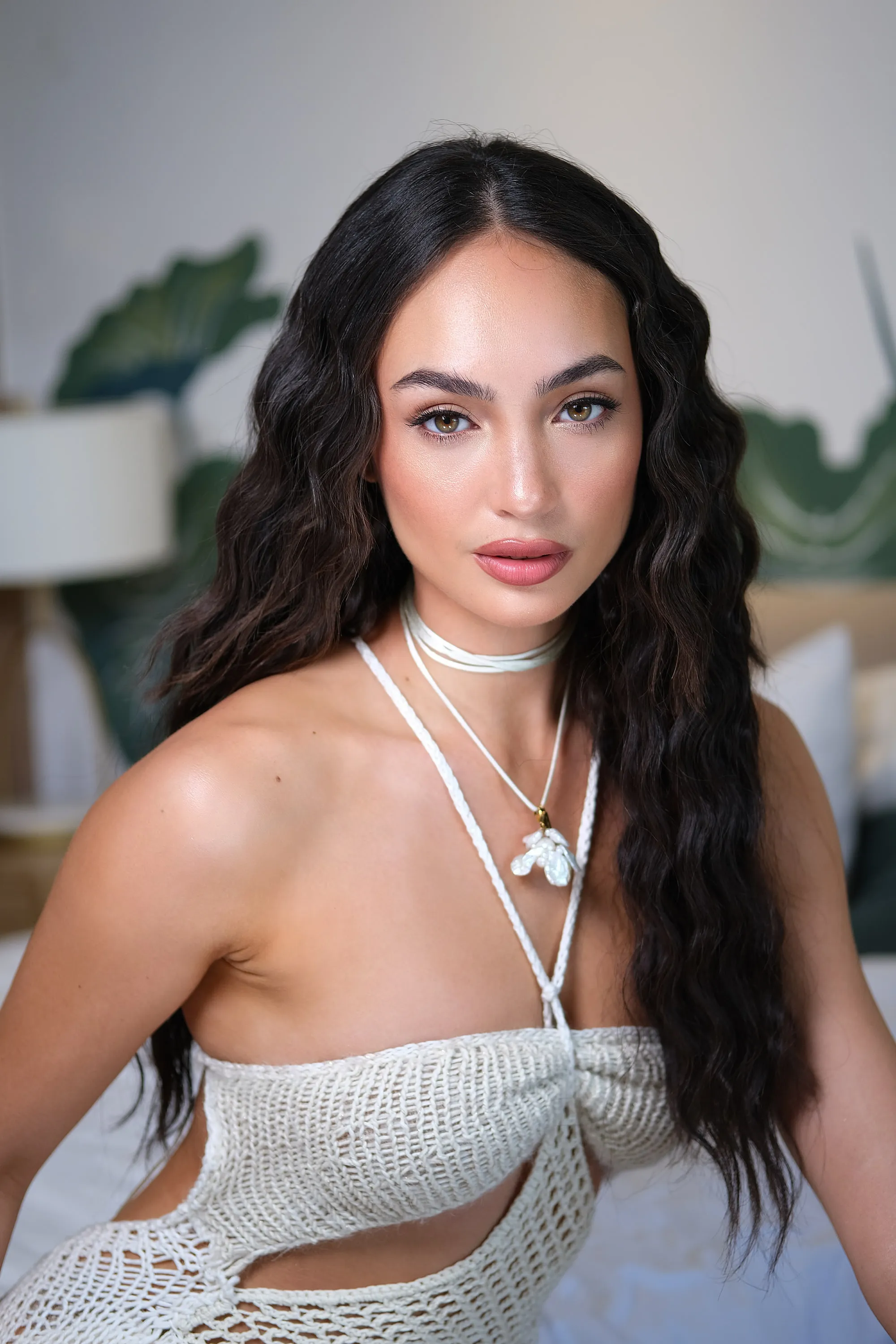 Editorial make-up with a high-shine skin finish and a warm nude lip, worn with long beach waves, a shell pendant and a crochet top.