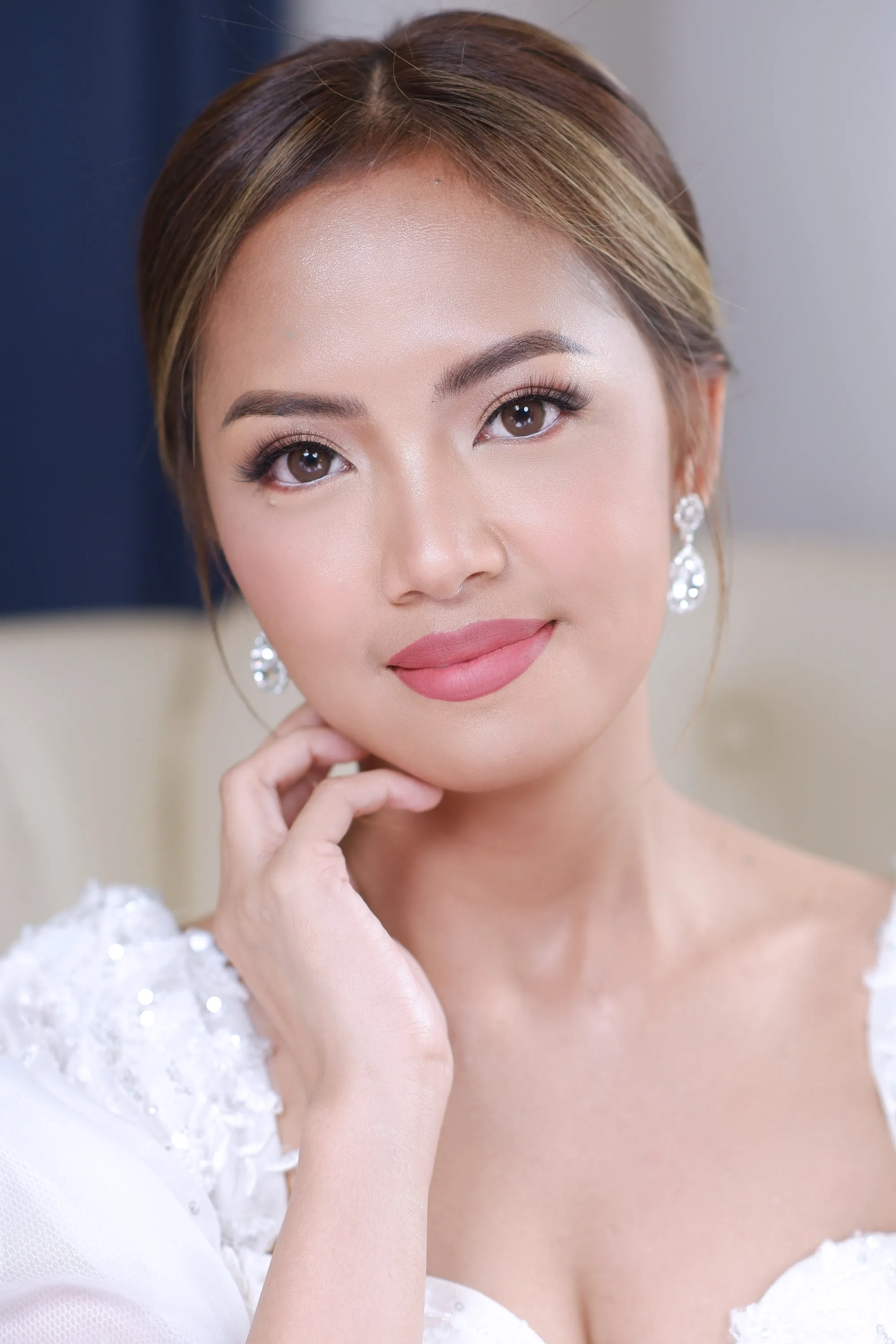 Bridal make-up with a deep pink lip and a bright highlight across the cheekbone, worn with teardrop earrings and a lace bodice.