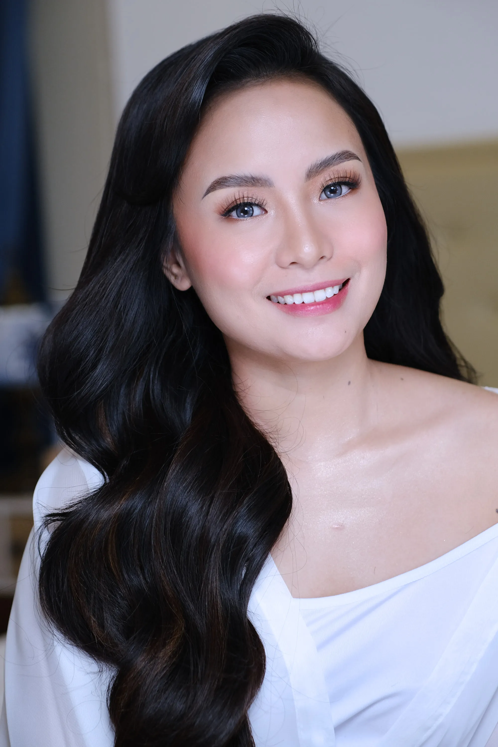 Bridal make-up with soft bronze shadow and a warm nude lip, worn with long dark waves and a white off-shoulder neckline.