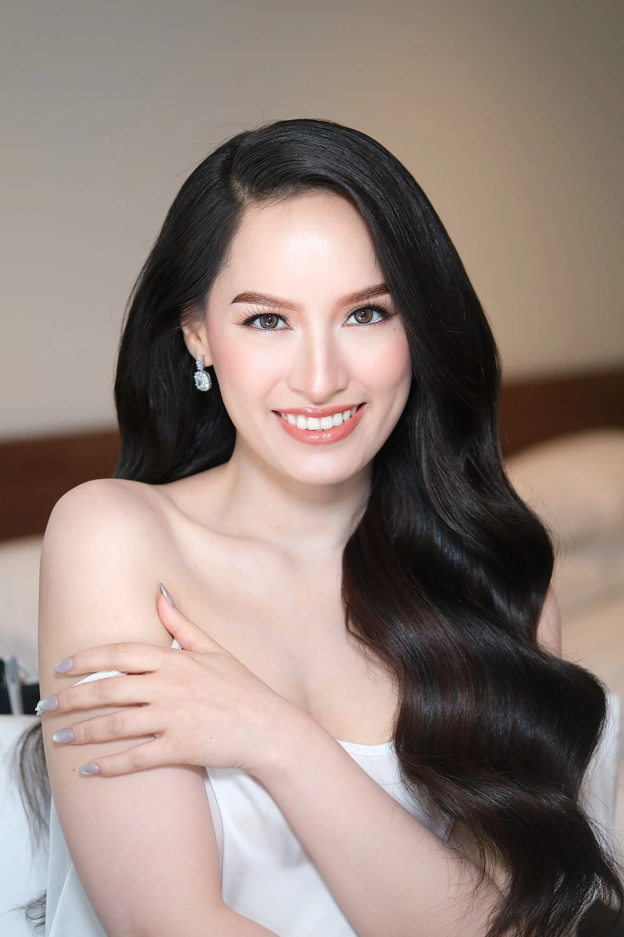 Bridal make-up with a coral lip and softly defined lashes, worn with glossy black waves over one shoulder.