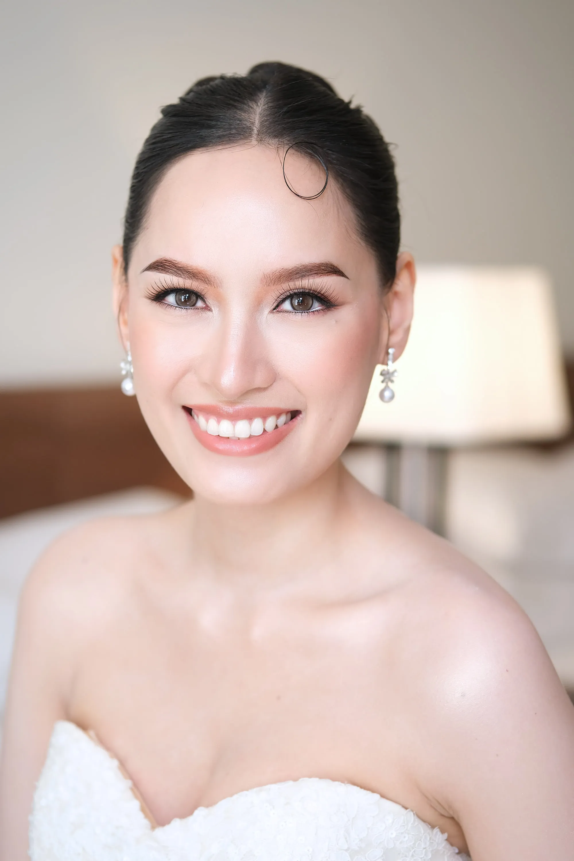 Bridal make-up with a soft brown shadow and a warm pink lip, worn with pearl drop earrings and a beaded gown.
