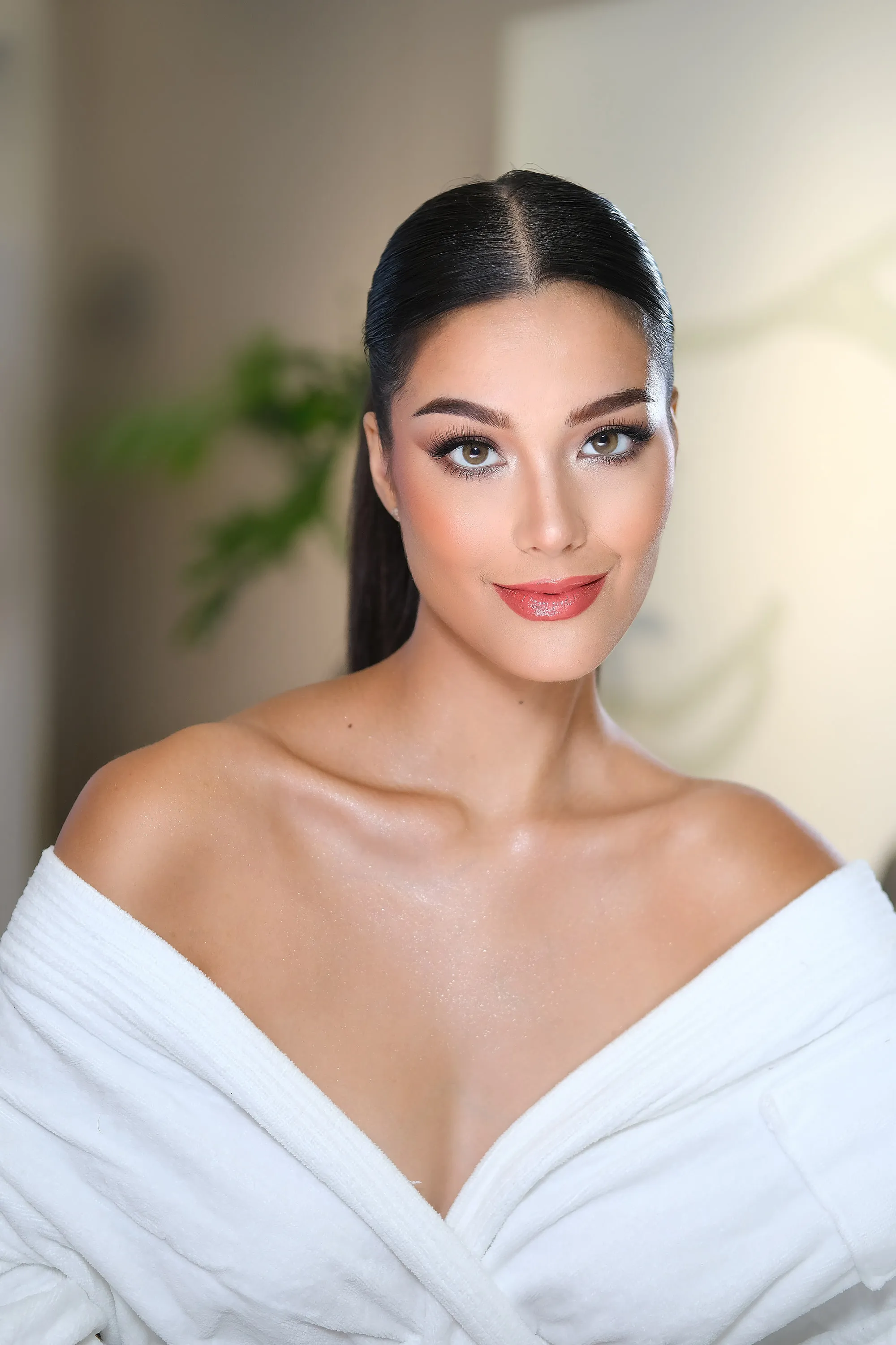 Pageant preparation make-up with a defined lash line and a soft coral lip, worn with a sleek centre part and a white robe.