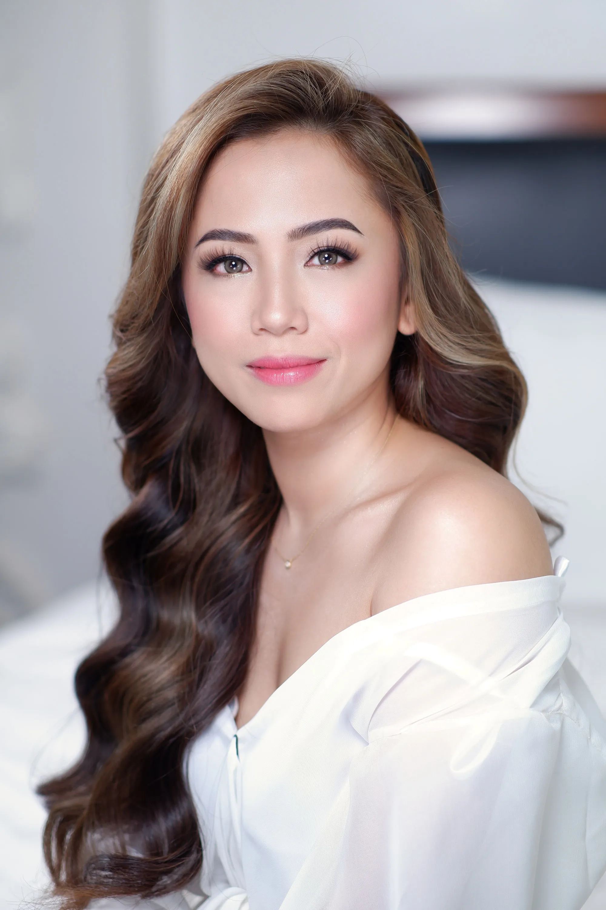 Bridal make-up with a strongly defined brow and a warm pink lip, worn with long waves and a white off-shoulder neckline.