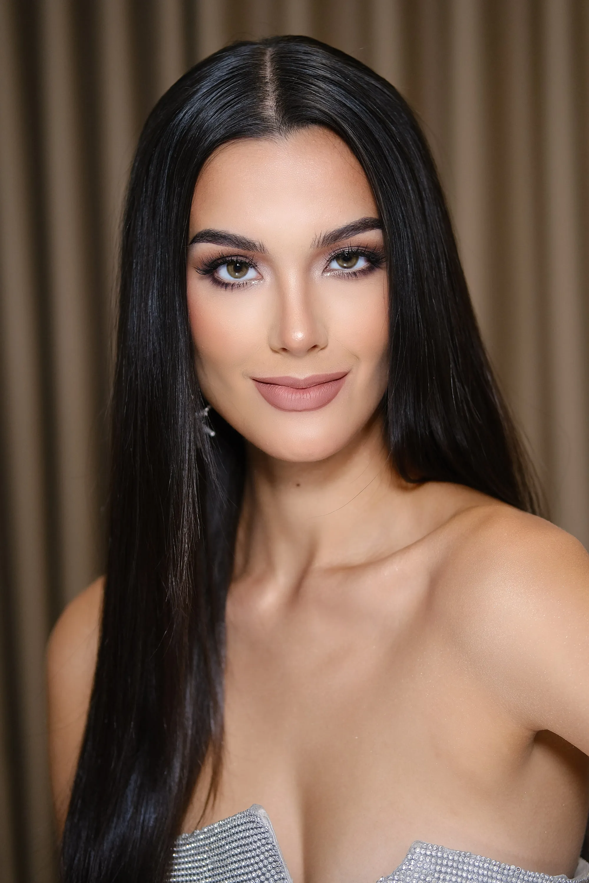Beauty make-up with a taupe shadow, a strong brow and a nude lip, worn with long straight hair and a silver bodice.
