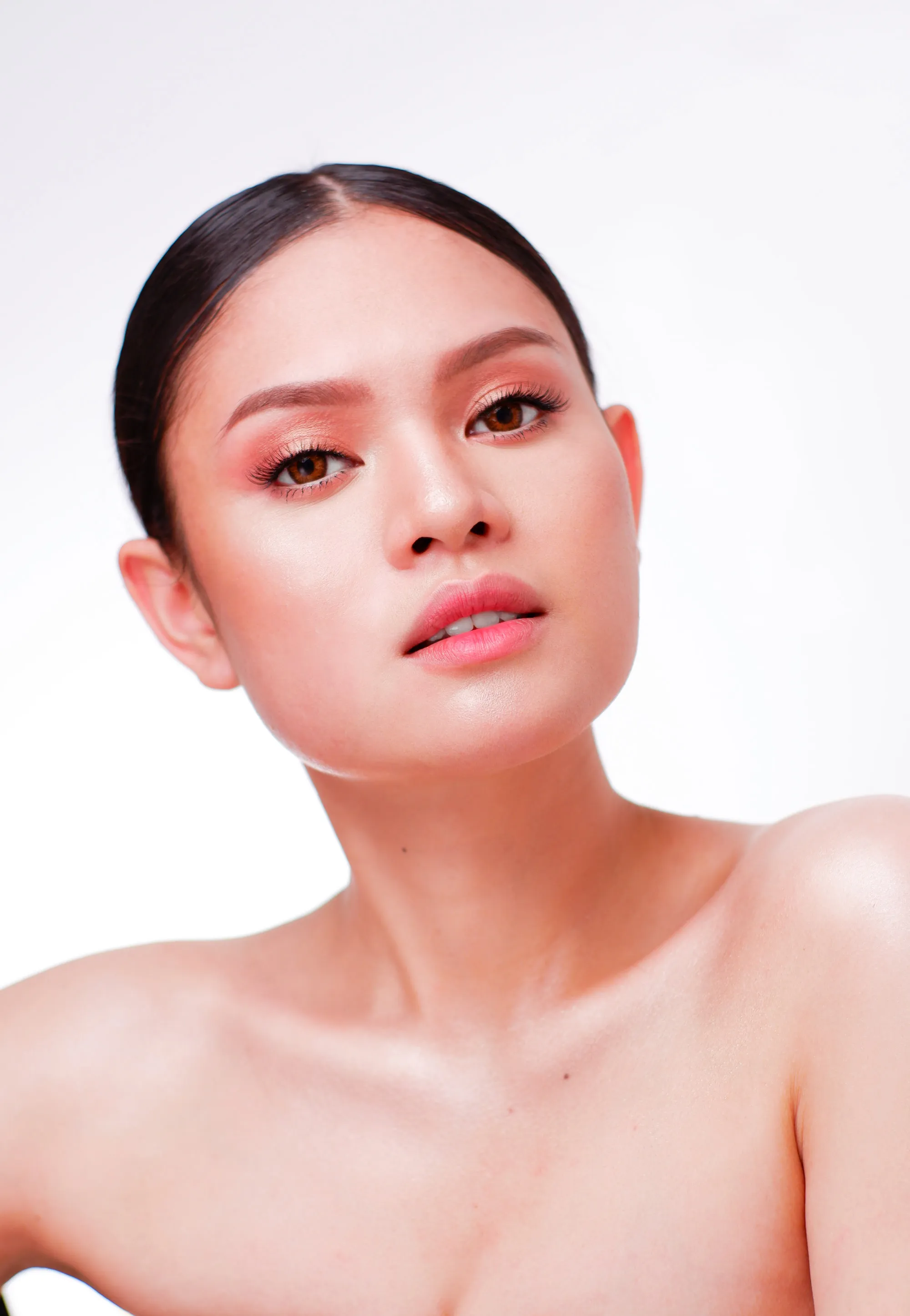 Studio beauty look with a warm coral eye blended to the brow bone and a matching coral lip, worn with the hair swept flat and back.