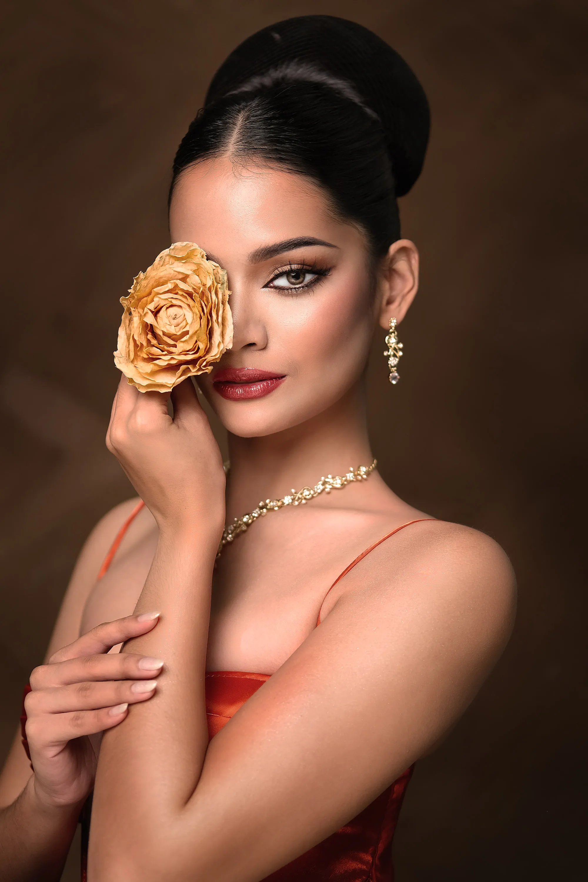 Editorial make-up with a smoky gold eye, sharp liner and a deep berry lip, photographed against a dark ground with a preserved gold rose held to one cheek.